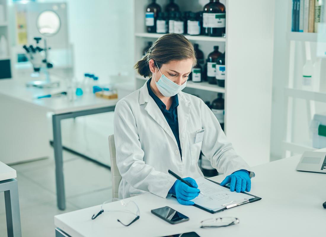 a masked female scientist filling out paperwork in a laboratory