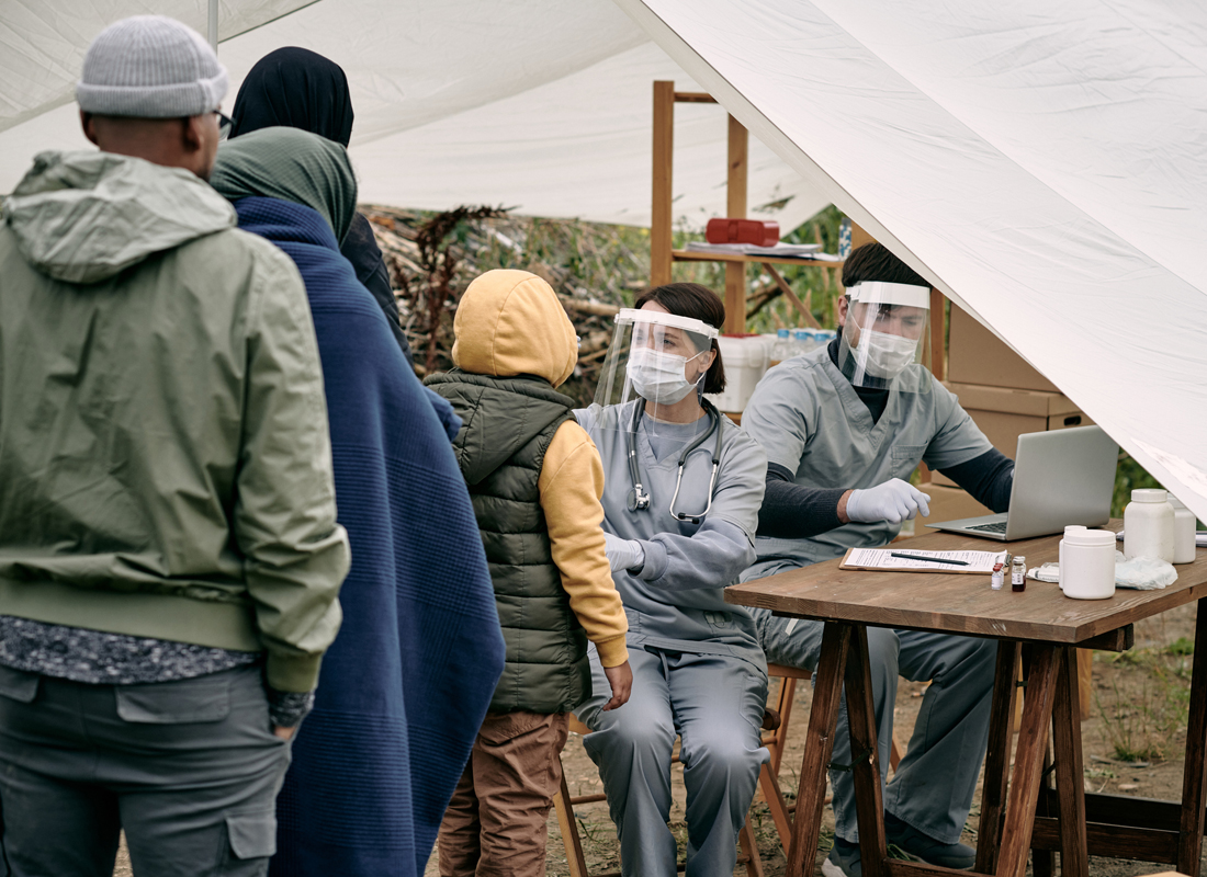 A healthcare worker in personal protective equipment offers a kit to an unhoused individual.