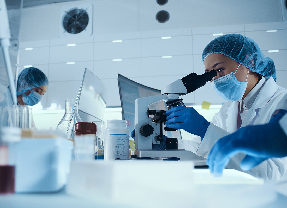Laboratory in full PPE looks through a microscope at a lab bench with several computer monitors, illustrating a digital pathology concept