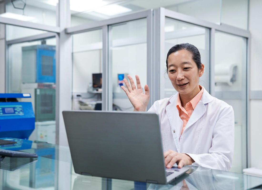 Female medical worker doing video call via a laptop at her desk in the laboratory, illustrating the concept of remote laboratory recruitment.