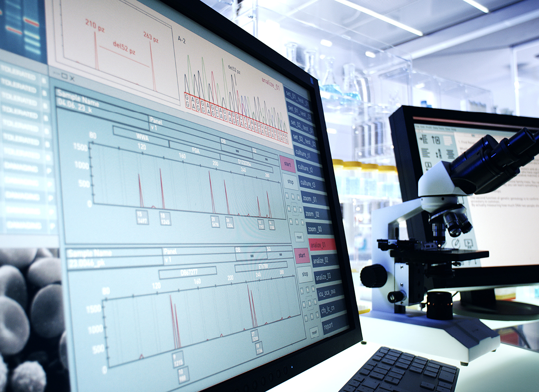 A close-up of laboratory technology, including multiple computer screens, a DNA sequence readout, and an optical microscope