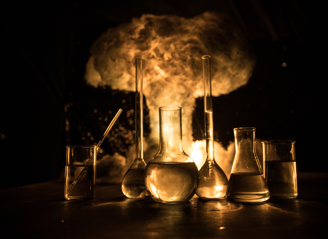 An assortment of laboratory glassware set against the backdrop of a mushroom cloud.