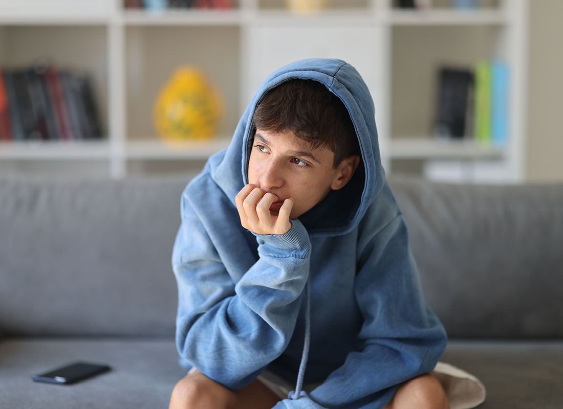Teen in hoodie looking off with fingers near his mouth